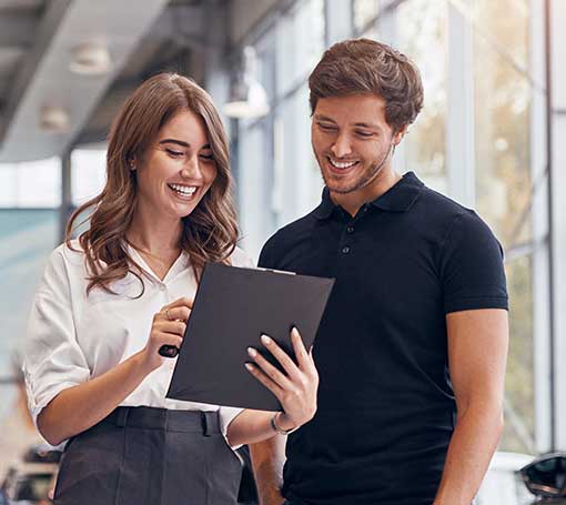 positive young professional saleswoman demonstrating document to male customer buying new car in dealership